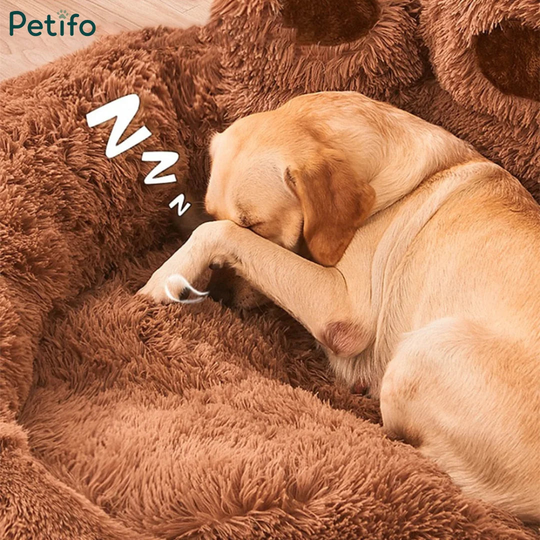 A golden retriever dozing off with its paw over its face inside a plush brown paw bed.