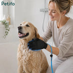 Woman happily bathing a golden retriever with a blue grooming glove in a bathtub.