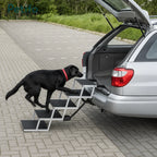 Black Labrador walking up a portable metal folding dog stair ramp attached to a silver SUV trunk.