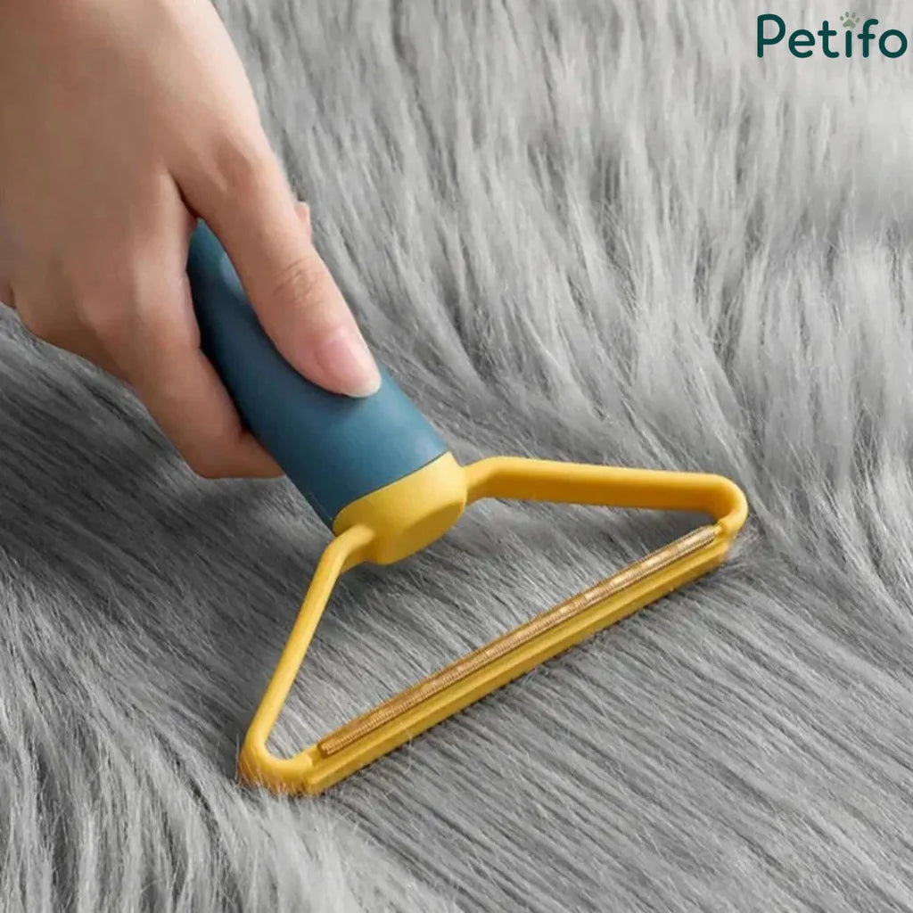 A hand using a blue and yellow pet lint remover on a fluffy gray rug.