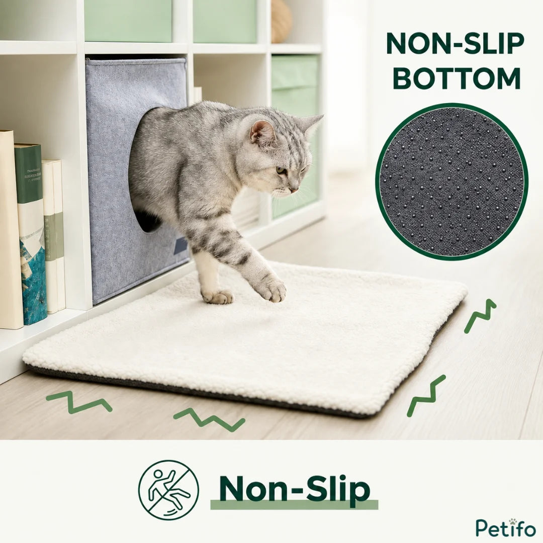 A grey tabby cat stepping out of a fabric cube pet house onto a white fluffy mat, accompanied by a circular zoom-in feature showing the non-slip dotted bottom and text reading "NON-SLIP BOTTOM".