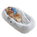 Woman sleeping comfortably inside a large grey human dog bed next to a golden retriever.