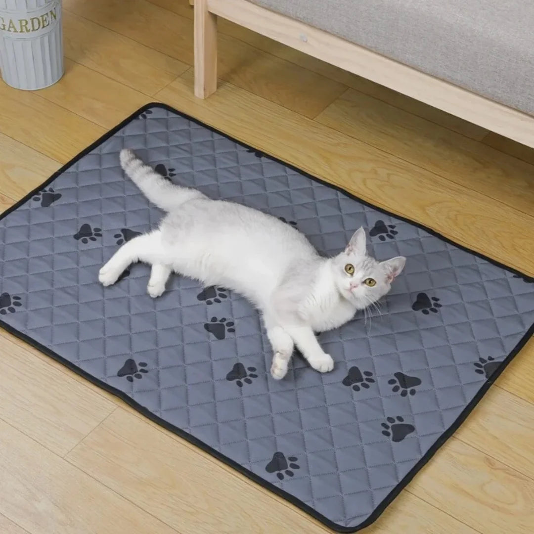 A white cat lying comfortably on a grey quilted washable pet training mat placed on a wooden floor.