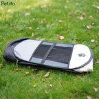 Compact folded Petifo portable dog playpen lying flat on a green grass lawn.