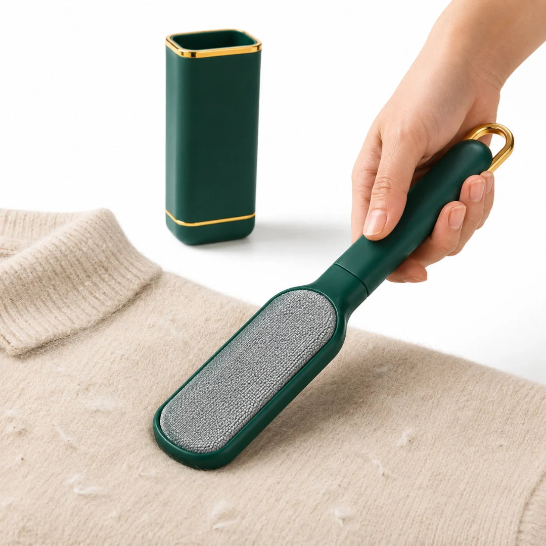 Hand holding a dark green and gold lint remover brush next to its matching self-cleaning base while cleaning lint off a beige sweater.