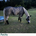 Light grey horse grazing in a grassy field while wearing a black mesh fly sheet and matching leg wraps.