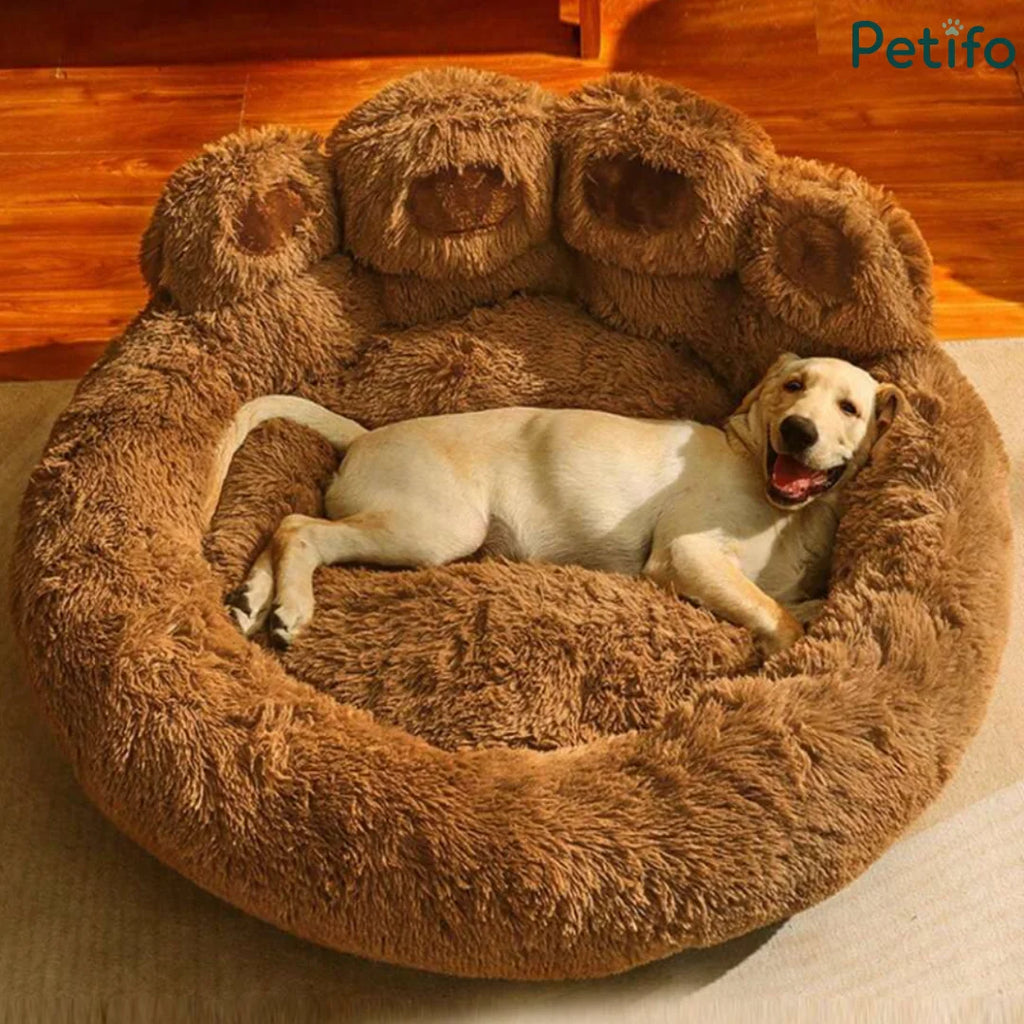 A golden retriever resting comfortably inside a large, plush brown paw-shaped dog bed.