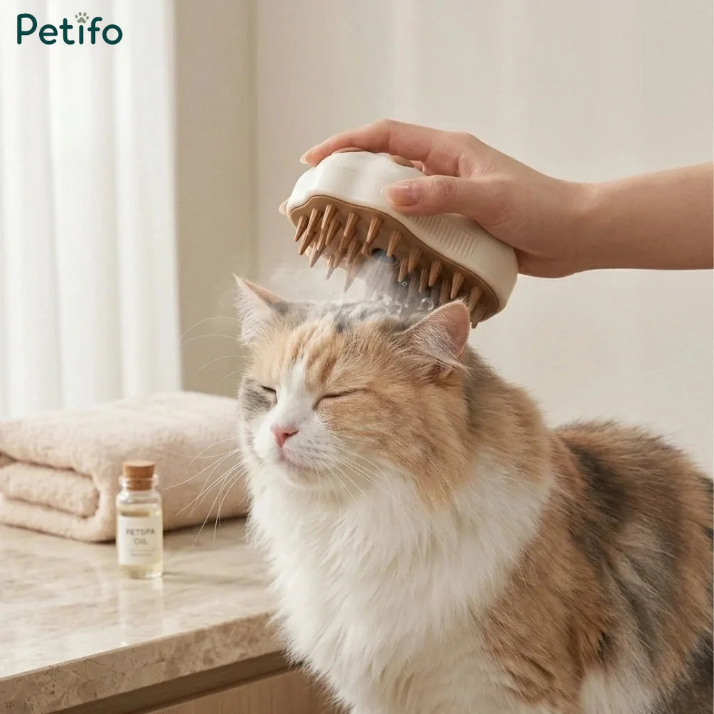 A person using a steaming paw-shaped massage brush on a fluffy calico cat's head.