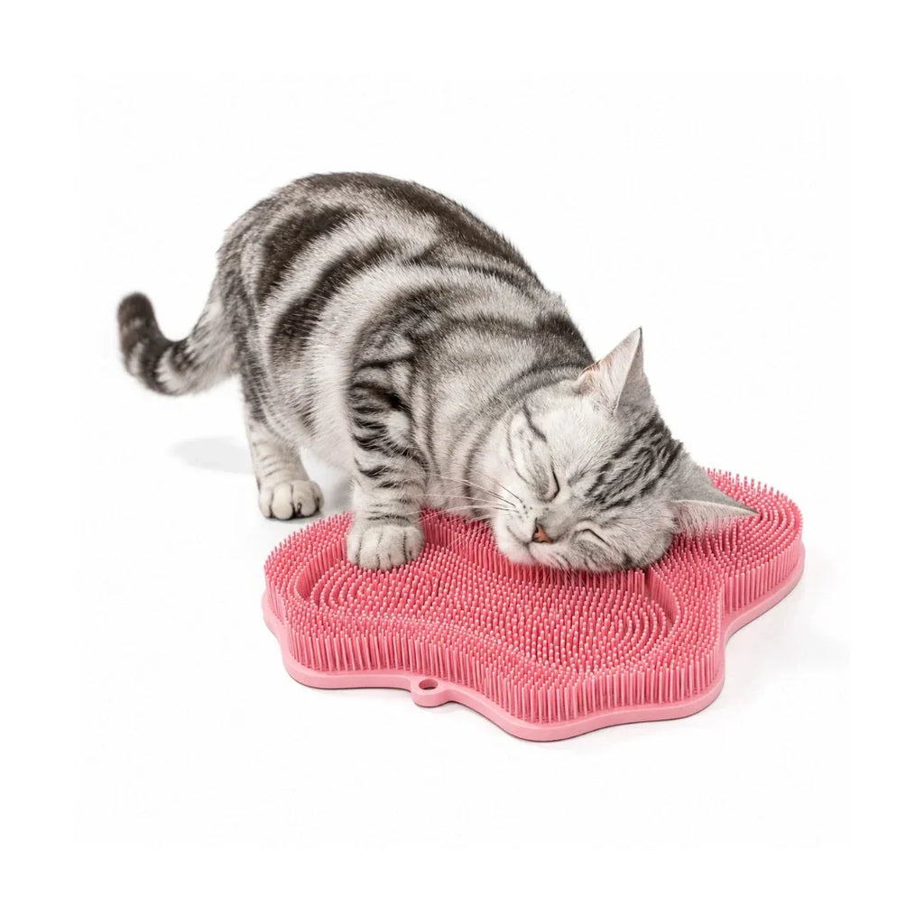 A gray tabby cat with closed eyes rubbing its head and face blissfully on a pink paw-shaped silicone self-groomer pad.
