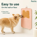 Cute dog licking peanut butter off a wall-mounted pink Petifo slow feeder lick mat